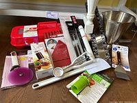 Photo showing a variety of baking tools including a perforated cutting wheel, cupcake injector/decorating set, spatulas, scraper, measuring spoons, pastry roller, and metal mixing bowl.