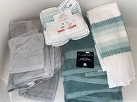 Grouped bathroom towels including Caro four-piece set with tags, Mirabella bath towels, and others in gray and white with teal stripe patterns, displayed in bathtub.