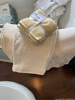 Yellow textured washcloths tied with white ribbon, sitting on off white Tommy Hilfiger bath towel with Greek key border