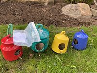 Photo of all 4 ceramic bird feeders in red, turquoise, yellow, and blue colors, showing shape, openings, and perches on grass outdoors.