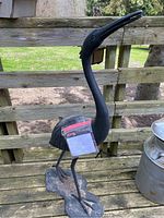 Full view of black metal crane garden sculpture standing on a deck railing.