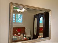 Front view of rectangular wall mirror with carved, off-white frame reflecting room interior.