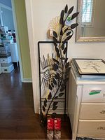 Black metal branch wall art with multiple oval leaves, next to yellow flower-shaped garden stake and two unopened boxes of lawn stakes