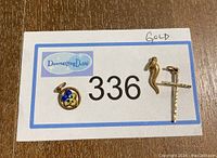 Photo of three gold pendants on a lot number tag for size reference