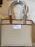 Full front view of Michael Kors tote handbag with protective wrapping on straps and a lot tag number 12.