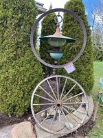 Front view of entire metal garden bird feeder mounted on decorative wagon wheel stand in garden setting