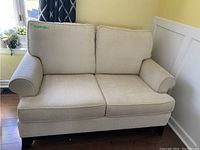 Front view of cream loveseat showing upholstery, armrests, cushions and overall condition.