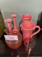Overview of lot with pink ceramic and glassware pieces including pitcher, candle holders, vase, glass container.
