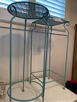 Two blue metal plant stands, one round top and one square top, shown side by side against a window background.