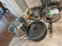 Photo showing all pots and saucepans including Bergner, Kirkland, Chefs Pride Series 3000, Palm Restaurant, and Aaron Sanchez pieces on wooden floor.