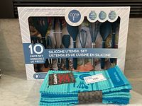 Front view of the sealed box containing 10 silicone kitchen utensils with a 5-pack of blue Cuisinart kitchen towels in front
