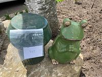 Both frog statue and mushroom stool side by side on stone surface with identification tag visible
