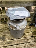 Full view of the vintage metal milk can placed on a wooden deck, showing overall condition and lid placement.