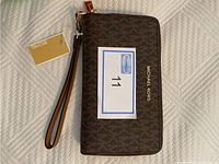 Top view of the brown Michael Kors clutch with wrist strap and brand name on front.