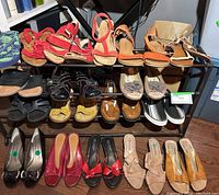 Wide view showing multiple pairs of shoes arranged on a three-tier metal shoe rack including strappy red sandals, flats, and slip-ons.