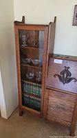 Front view of tall narrow oak display cabinet with glass door, three glass shelves and books on bottom shelf