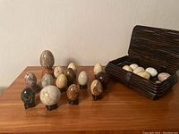 Multiple stone and crystal eggs and spheres of different colors and sizes arranged on a wooden surface and inside a wicker basket