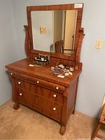 Front view of wooden dresser with large attached mirror showing three drawers with white knobs and curved legs.
