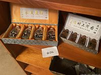 Overall view showing two sets of Chinese decorative glass vials in presentation boxes, placed on wooden furniture.