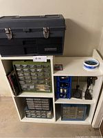 Photo showing entire shelving unit with toolbox on top and three hardware organizers inside compartments alongside small workshop items.