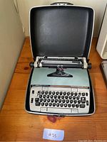 Smith Corona typewriter open inside the hard case, visible keyboard and carriage with paper loaded.