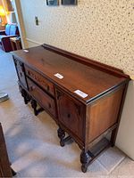 Solid wood buffet table angled front view showing carved drawer and doors, turned front legs.