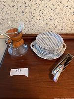Lot arrangement of six Victorian-style pottery plates stacked with two handled pottery tray beneath, glass decanter with wooden collar and leather strap, and decorative cutting utensils in a box alongside.