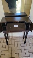 Front view of vintage small wooden desk showing top section with drop-down writing surface and two side cabinets closed