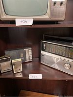 Four vintage audio electronics items on display shelf, including three radios and one tape player.