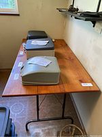 Folding wooden table top and metal legs with several items placed on top, taken from an angle showing table top surface and legs.