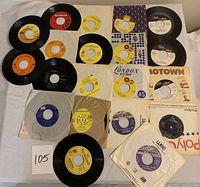 Top-down image showing 20 vintage 45 RPM vinyl records spread on a flat surface. Various record label colors seen including orange, yellow, white, purple, blue, and red. Several paper sleeves are visible including a 'London Records' sleeve and multiple Tamla Motown sleeves.