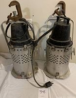 Two vintage aluminum stage light cans shown upright with attached clamps and power cords on white surface.