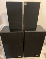 Front view of two Altec Lansing vintage speakers with black incomplete or damaged grills on top of a table against a white wall.