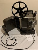 Bell & Howell Super 8 projector unit with large reel arm, power cord attached, and control knobs visible. Projector is open and placed on white surface.