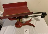 Side view of the antique red and gold Fairbanks Morse fishtail scale showing the weighing platform, base, and the sliding weight measurement arm.