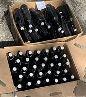 Two cardboard boxes containing approximately 80 dark amber glass bottles with white flip-top lids. Bottles appear dusty on outsides but clean inside.