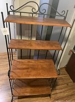 Front view of bakers rack showing four oak shelves and wrought iron frame with scrollwork detail.