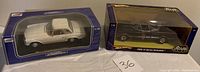 Two boxed 1:18 scale model cars: white Mercedes 280SL and black 1966 Batmobile side by side.