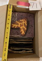 Top view of a box with stacked 45 RPM records, showing a 'Talk Talk' record cover on top about 7 inches tall within the box.