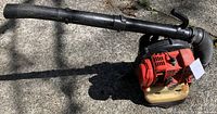 Side view of Shindaiwa backpack leaf blower showing red housing, yellow fuel tank, and attached black blowing tube.