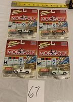 Four Johnny Lightning Monopoly collectible cars in sealed packaging, each including an exclusive game token. The cars are a black and white police car, an orange race car, a white delivery truck, and a light green delivery truck.