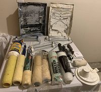 Painting tools including roller covers, frames, paint trays, and cloth rags spread on a surface