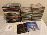 Photo showing two stacks of DVDs and CDs: one with music DVDs featuring various artists and the other a stack of radio station sampler CDs from 80s-90s Warner Music and A&M labels.