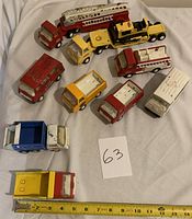 Photo showing 11 vintage metal Tonka trucks on white fabric surface, includes 11" fire ladder truck and various smaller trucks in red, yellow, blue, and white.