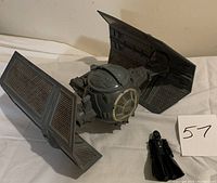 Darth Vader action figure standing next to TIE Fighter vehicle on a white surface with a number 57 card.