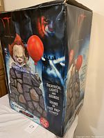 Photo of the box showing Pennywise pop-up Halloween prop with theatrical lights and sounds, sound or foot pad activation, and box damage from dampness.