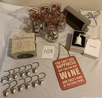 Photo of 12 shower curtain hooks, 7 Coca Cola polar bear tumblers, oil lamp new in box, tin sign, Pandora bell ornament, and untested lamp without bulb all arranged on a white sheet.