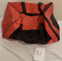 Side view of orange soft collapsible pet carrier with black mesh sides and handles, showing top zipper opening.