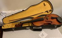 Open violin case showing the violin, bow, and yellow felt lining with some wear marks