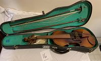 Violin and accessories inside an open case showing violin body, bows, and rosin with spare parts.
